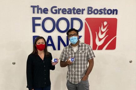 Two GBFB Team Members smiling at the camera, in masks holding grocery cards