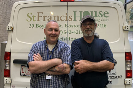 Two men standing with arms crossed, smiling at the camera