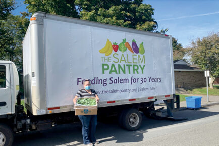 A Salem Pantry employee holding a box of food in front of a pantry truck