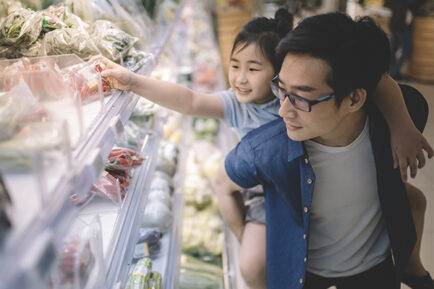 an asian chinese mid adult carrying his daughter at his back in supermarket buying tomatoes