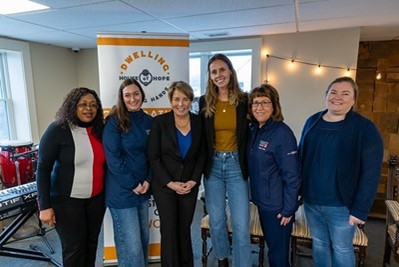 A group of women posed in front of a retractable baner with the Dwelling House of Hope logo visible at the top.