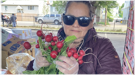 A woman in sunglasses holds a bushel of turnips outside a food donation site.