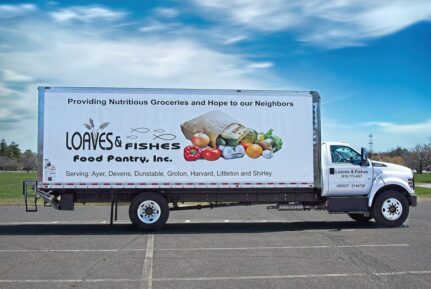 A white truck is parked in a parking lot with Loaves and Fishes food pantry on the side